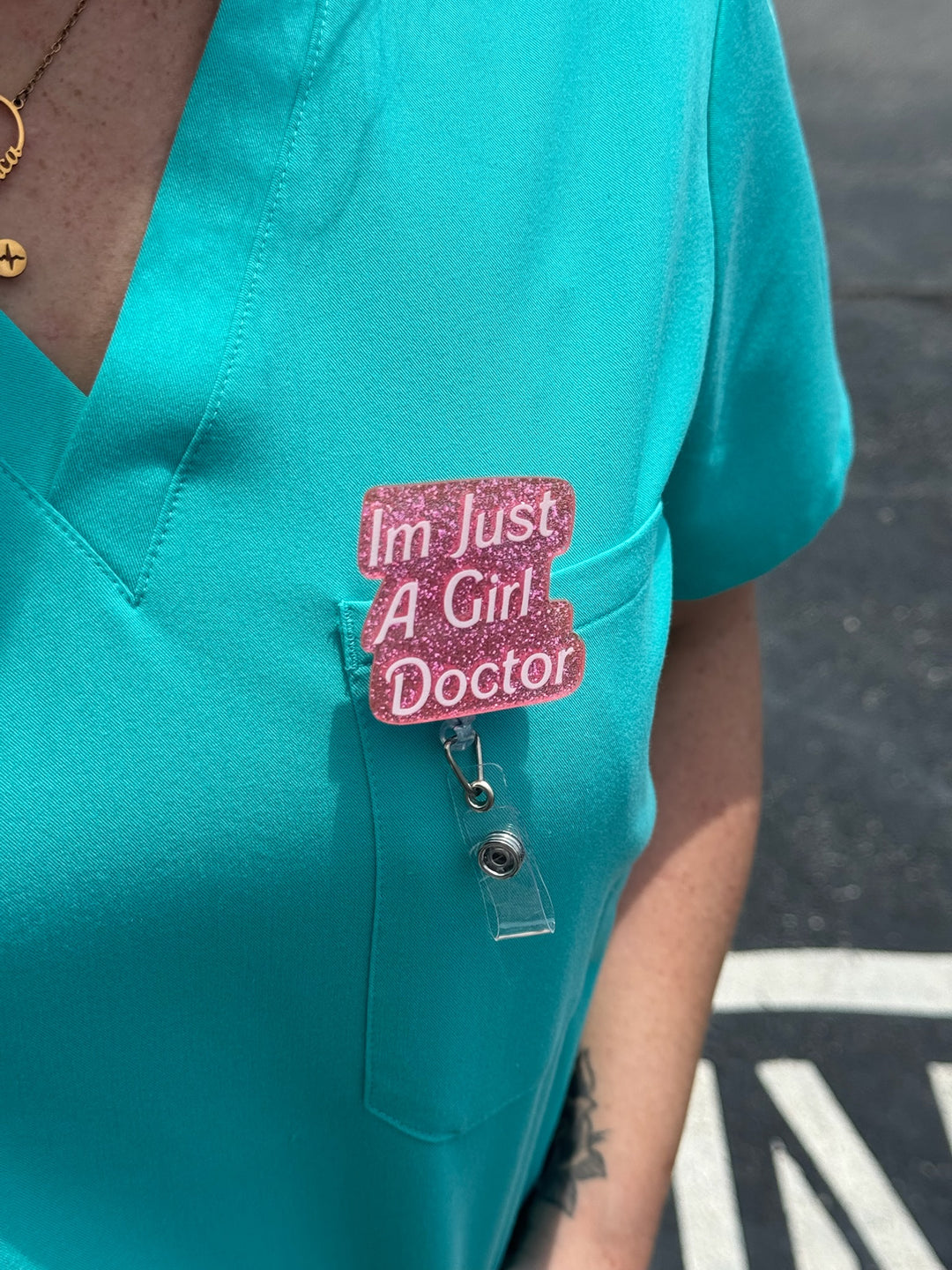 Woman wearing Ladyspinedoc x Dr. Daisy Collab: Pink "I'm Just A Girl Doctor" Badge Reel - Retractable with Alligator Clip on front back of scrubs