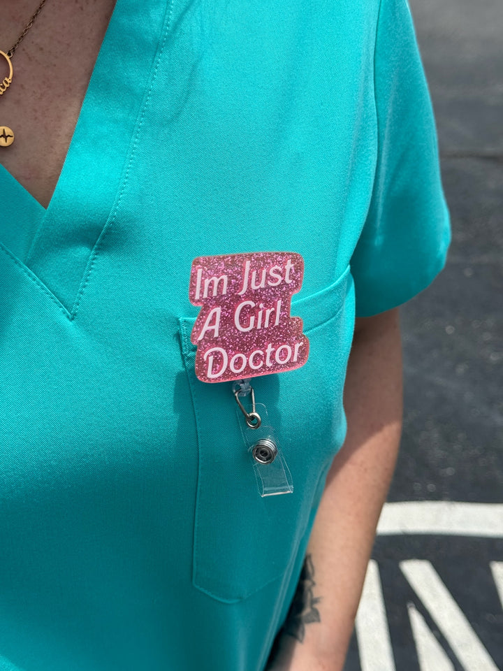 Woman wearing Ladyspinedoc x Dr. Daisy Collab: Pink "I'm Just A Girl Doctor" Badge Reel - Retractable with Alligator Clip on front back of scrubs