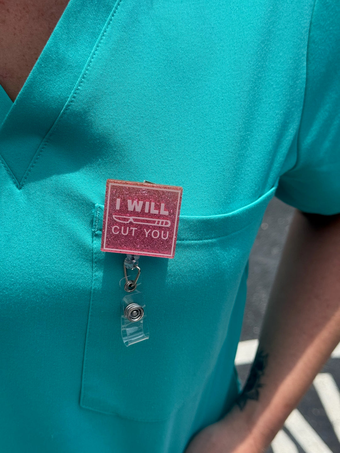 Dr. Daisy Collab: Pink "I WILL CUT YOU" Badge Reel clipped on aqua scrub shirt