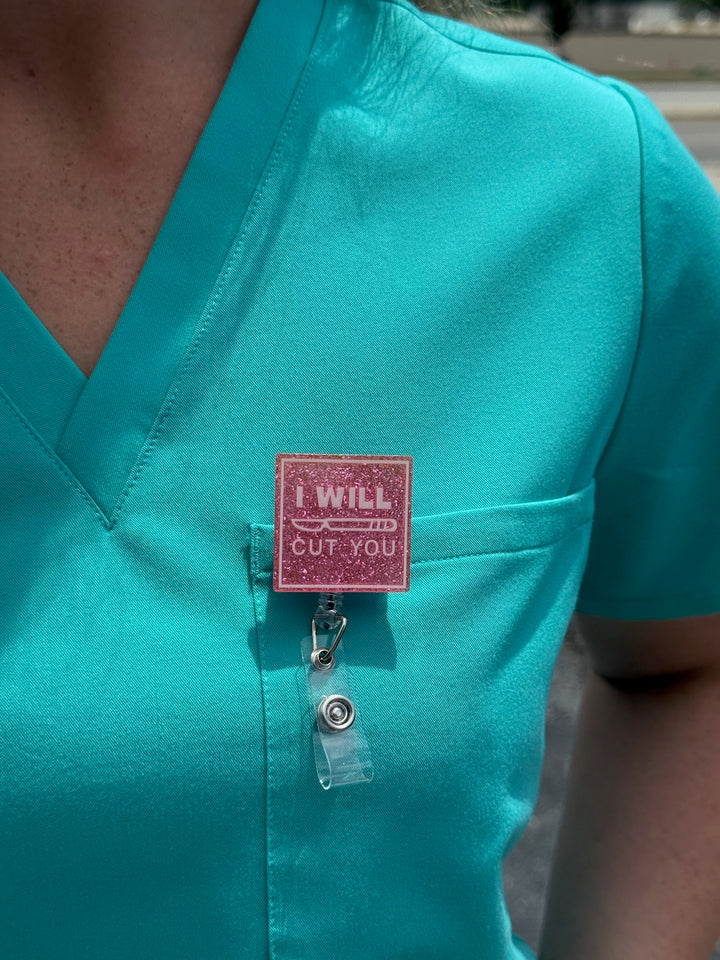Dr. Daisy Collab: Pink "I WILL CUT YOU" Badge Reel clipped on front pocket of aqua scrubs