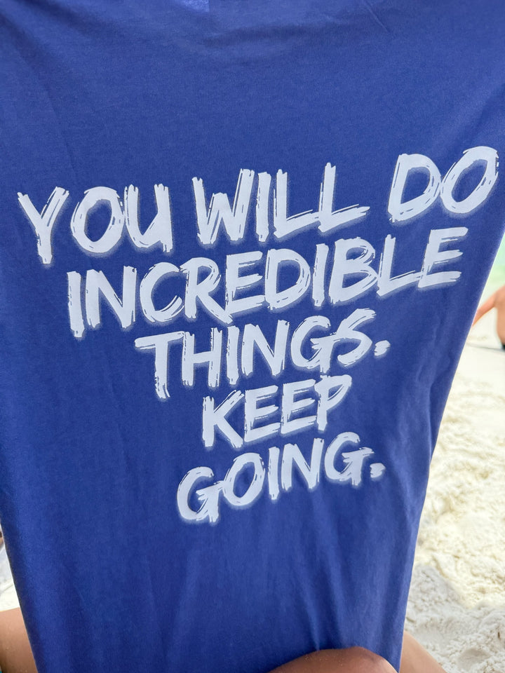 Back of the purple tee showing bold white text: “YOU WILL DO INCREDIBLE THINGS. KEEP GOING.”