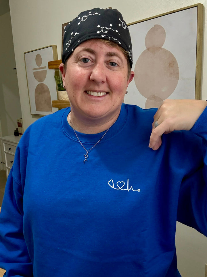 Dr. Beachgem wearing blue Heart of Medicine sweatshirt, showcasing her stethoscope and heart waveform logo
