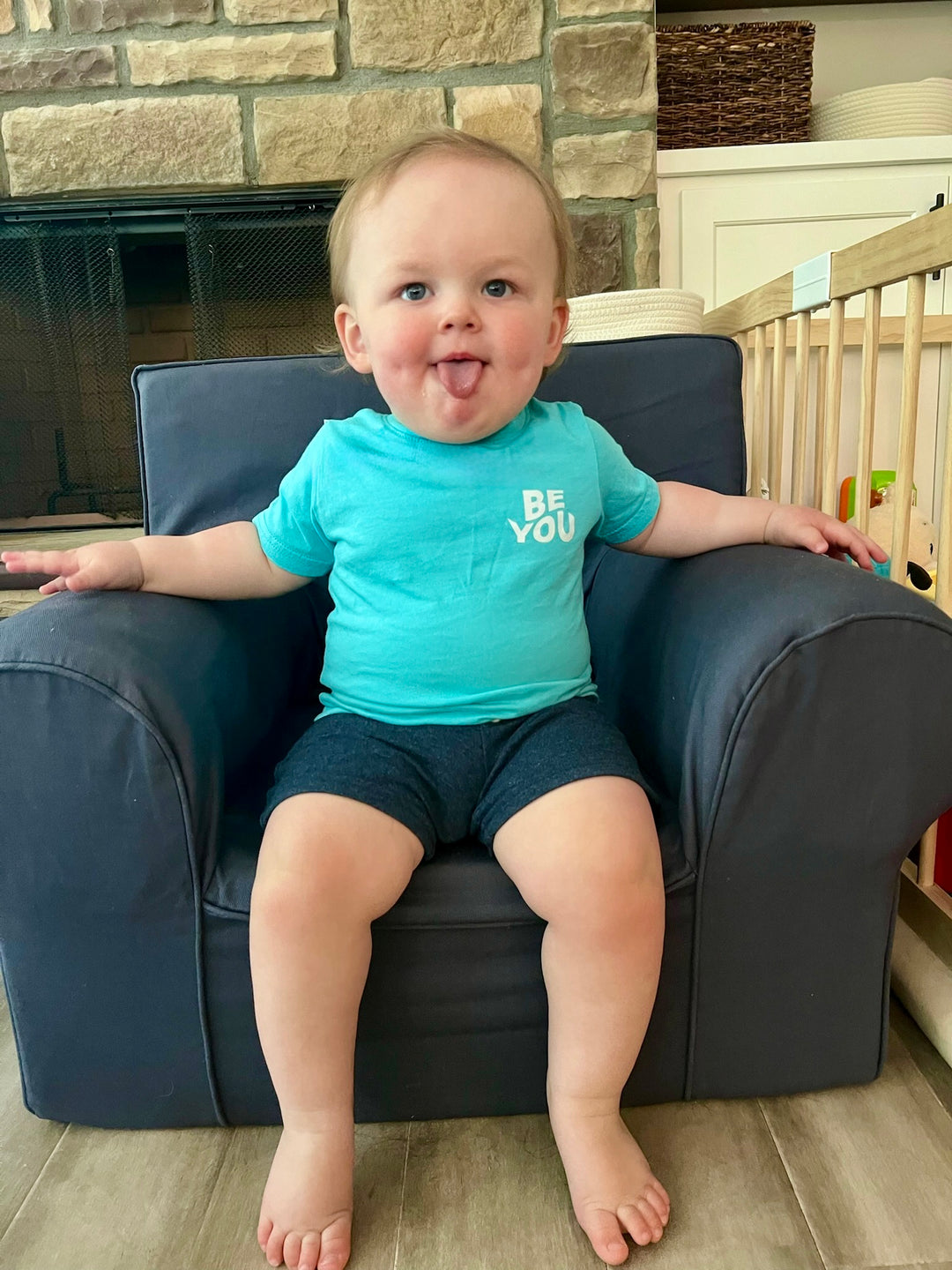 Sitting toddler with tongue out and wearing the Be You Toddler Tee - Kids Caribbean Blue T-Shirt, showing the BE YOU on the front upper left chest.