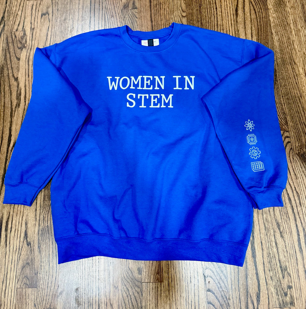 “Women in STEM” Sweatshirt laid flat on wood floor and showing the STEM icons of Science, Technology, Engineering, and Mathematics on the left sleeve.