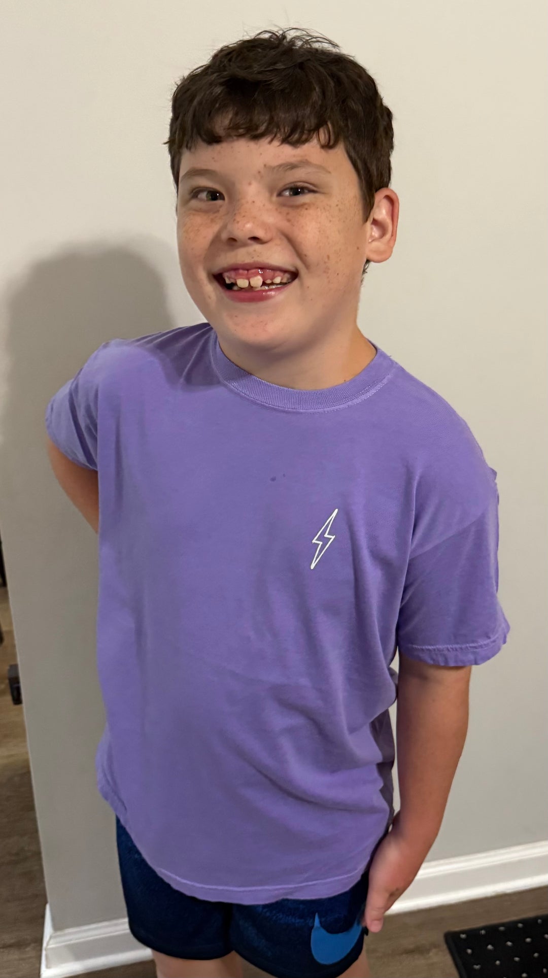 Boy wearing The Incredible Youth Tee – Violet Kids T-Shirt, showing the front with the Ladyspinedoc lightning bolt on upper left chest.