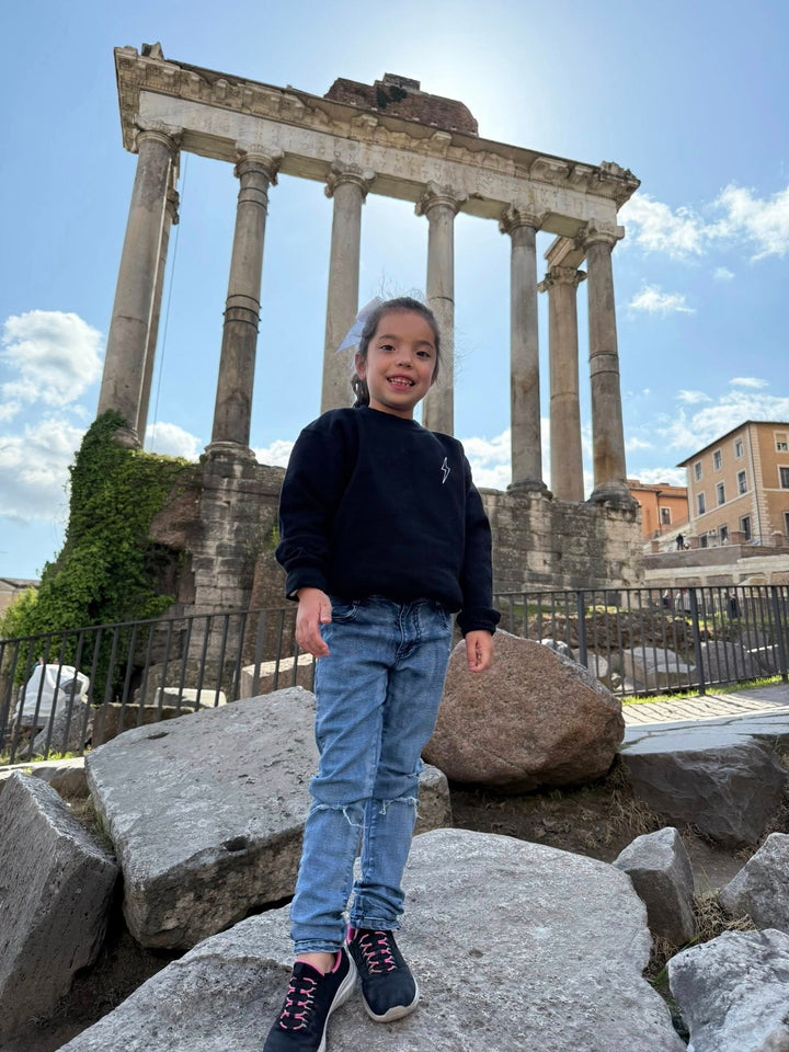 Front of young girl in Rome, Italy wearing the Kids Incredible Sweatshirt with Ladyspinedoc signature lightning bolt on the upper left chest.
