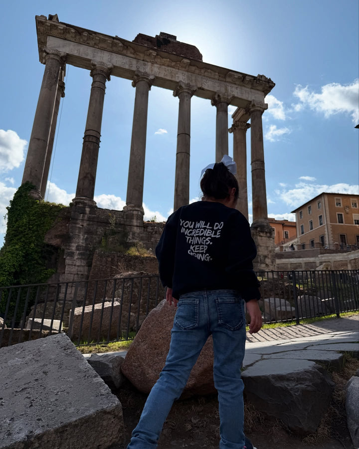 Back of young girl in Rome, Italy wearing the Kids Incredible Sweatshirt with "YOU WILL DO INCREDIBLE THINGS. KEEP GOING."  motto.