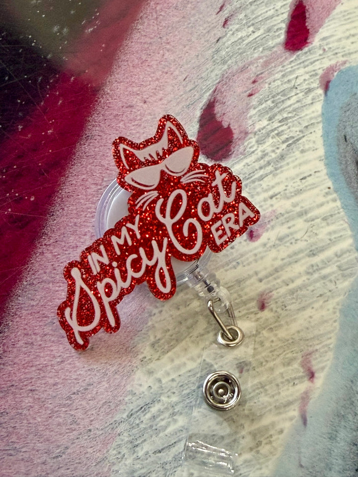 Red glittery 'I'm my cat's Spicy Cat' badge holder on a textured background