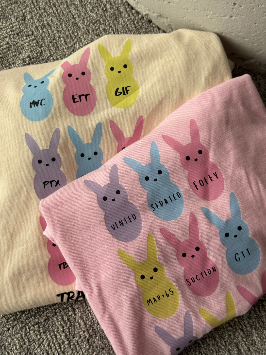 Folded  Trauma Squad and ICU Squad tee shirts with pastel bunny designs.