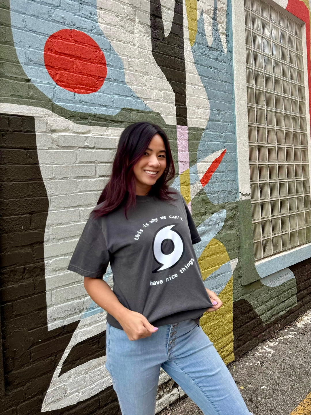 Woman wearing a dark gray t-shirt with a white hurricane logo in front of a colorful mural.