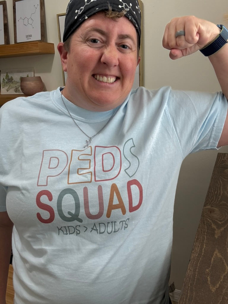 Dr. Beachgem wearing a t-shirt with 'Peds Squad' text, flexing her arm.