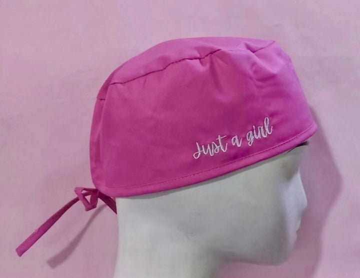 Pink tie back scrub cap with white embroidered 'Just a girl' text on a pink background