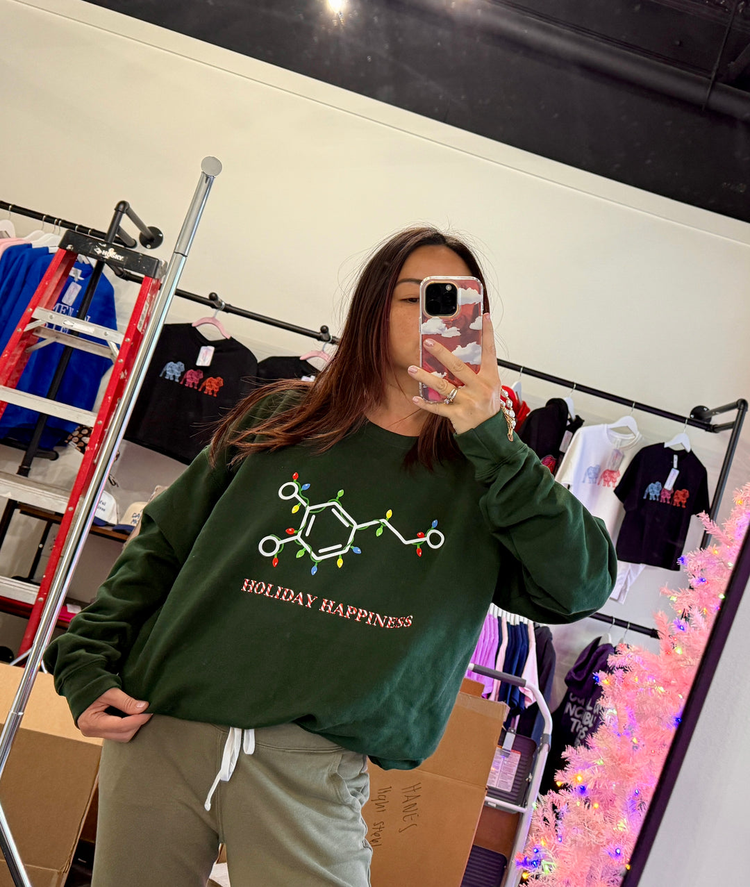 Woman wearing a green sweatshirt with a dopamine molecule covered in Christmas lights and  'Holiday Happiness' candy cane text underneath 
