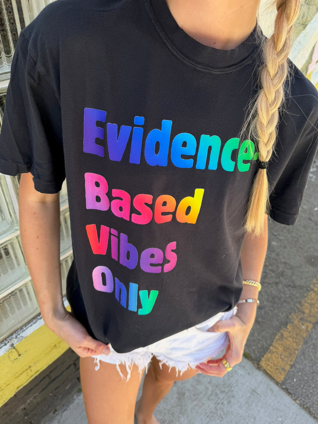 Person wearing a black t-shirt with colorful text 'Evidence-Based Vibes Only' on a street.