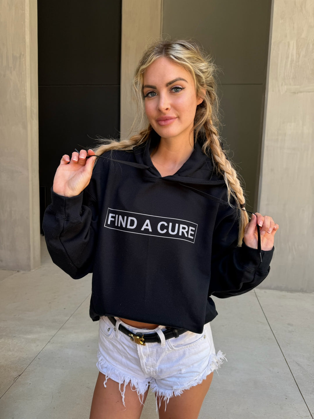 Woman wearing a black hoodie with 'Find a Cure' text, standing outdoors.