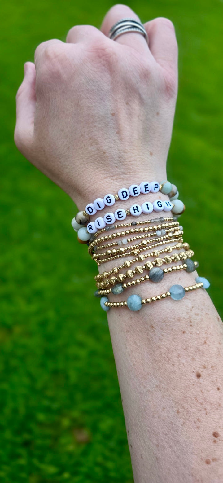 Model wearing multiple bracelets with motivational Dig Deep Rise High on a green background