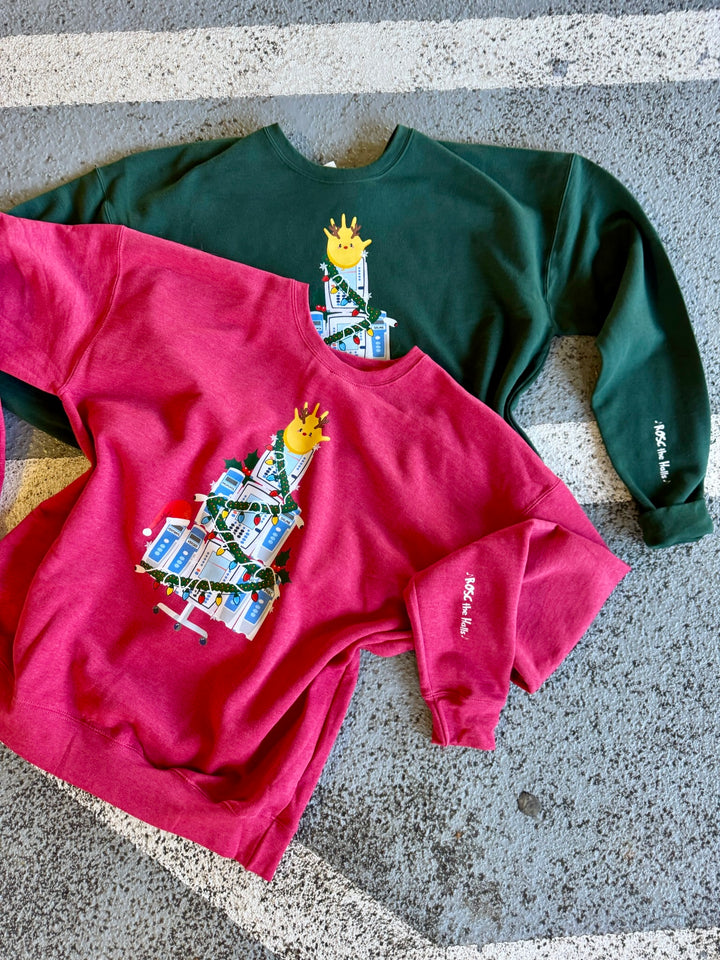 Two sweatshirts, one red and one green, with a IV Pump Christmas tree design and ROSC the Halls sleeve art, both on a concrete surface