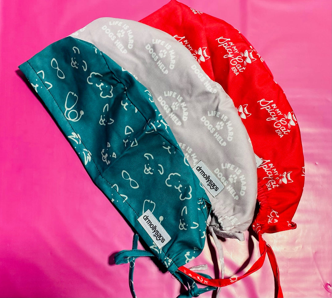Three scrub hats in green, gray, and red on a pink background