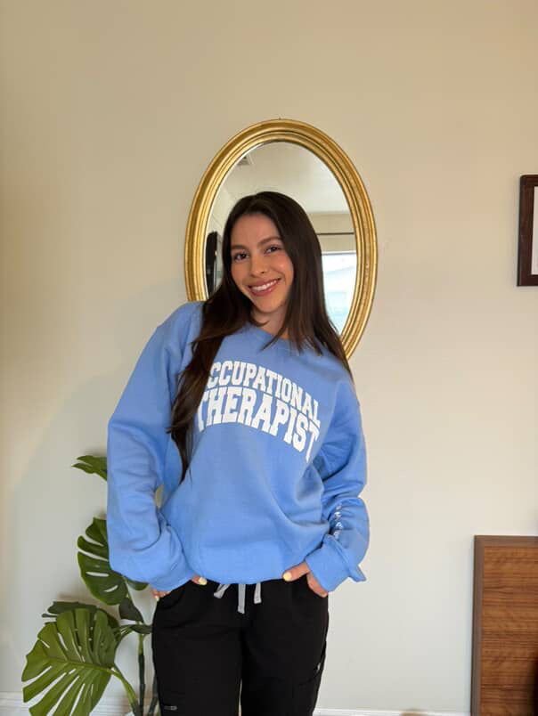 OT Sophie Perez wearing the blue Occupational Therapist sweatshirt designed by Ladyspinedoc (Dr. Betsy Grunch)
