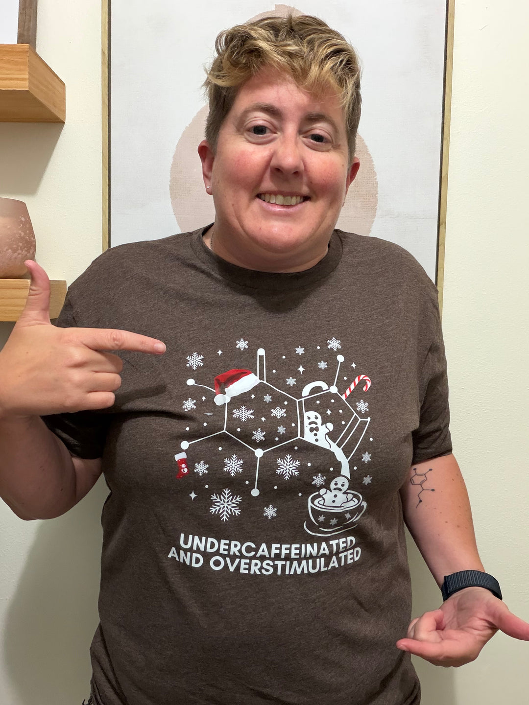 Dr. Beachgem wearing a brown holiday t-shirt with a graphic caffeine molecule design and text, pointing at the shirt.