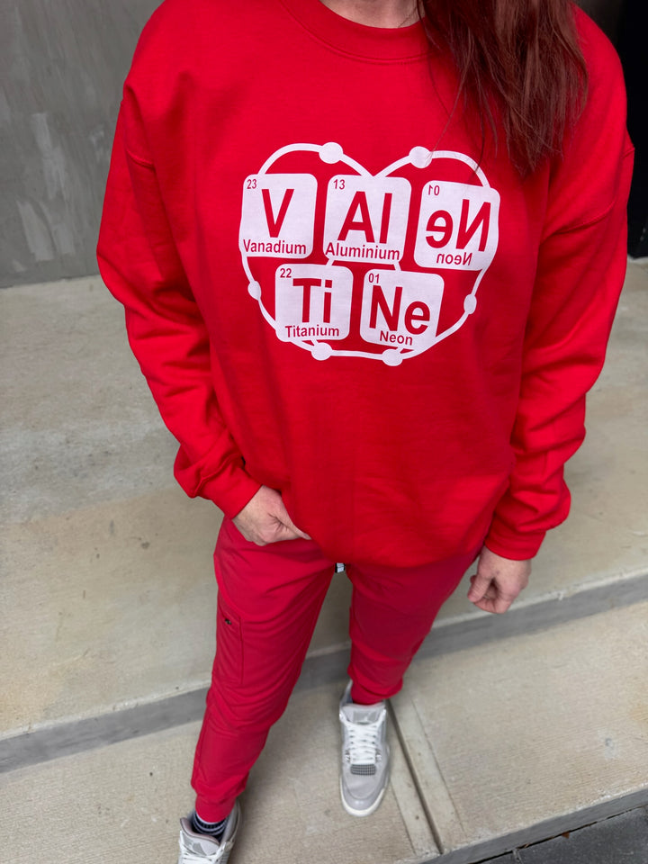 Ladyspinedoc wearing a red sweatshirt with Valentine periodic table design on a sidewalk.
