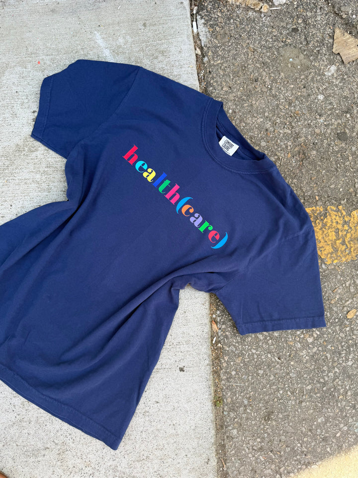 Blue t-shirt with 'health(care)' printed in colorful letters on a concrete surface.