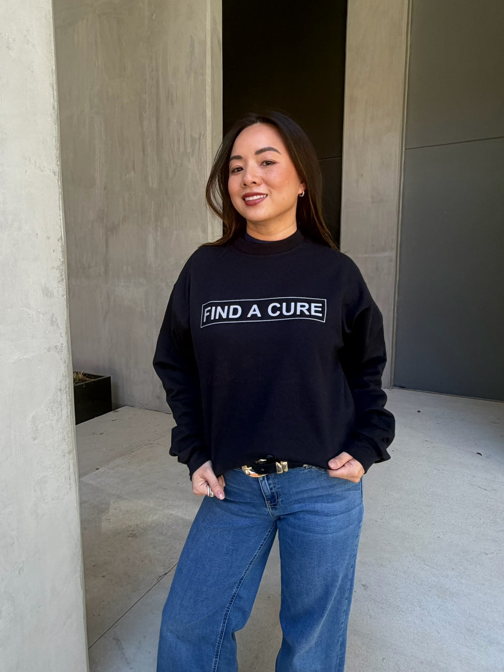 Person wearing a black sweatshirt with 'Find a Cure' text, standing in an outdoor setting.