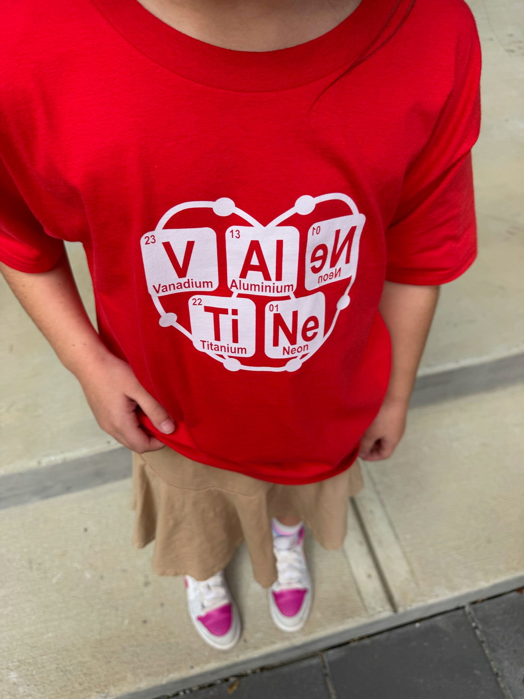 Child wearing a red periodic table Valentine shirt with a white graphic design on a sidewalk.