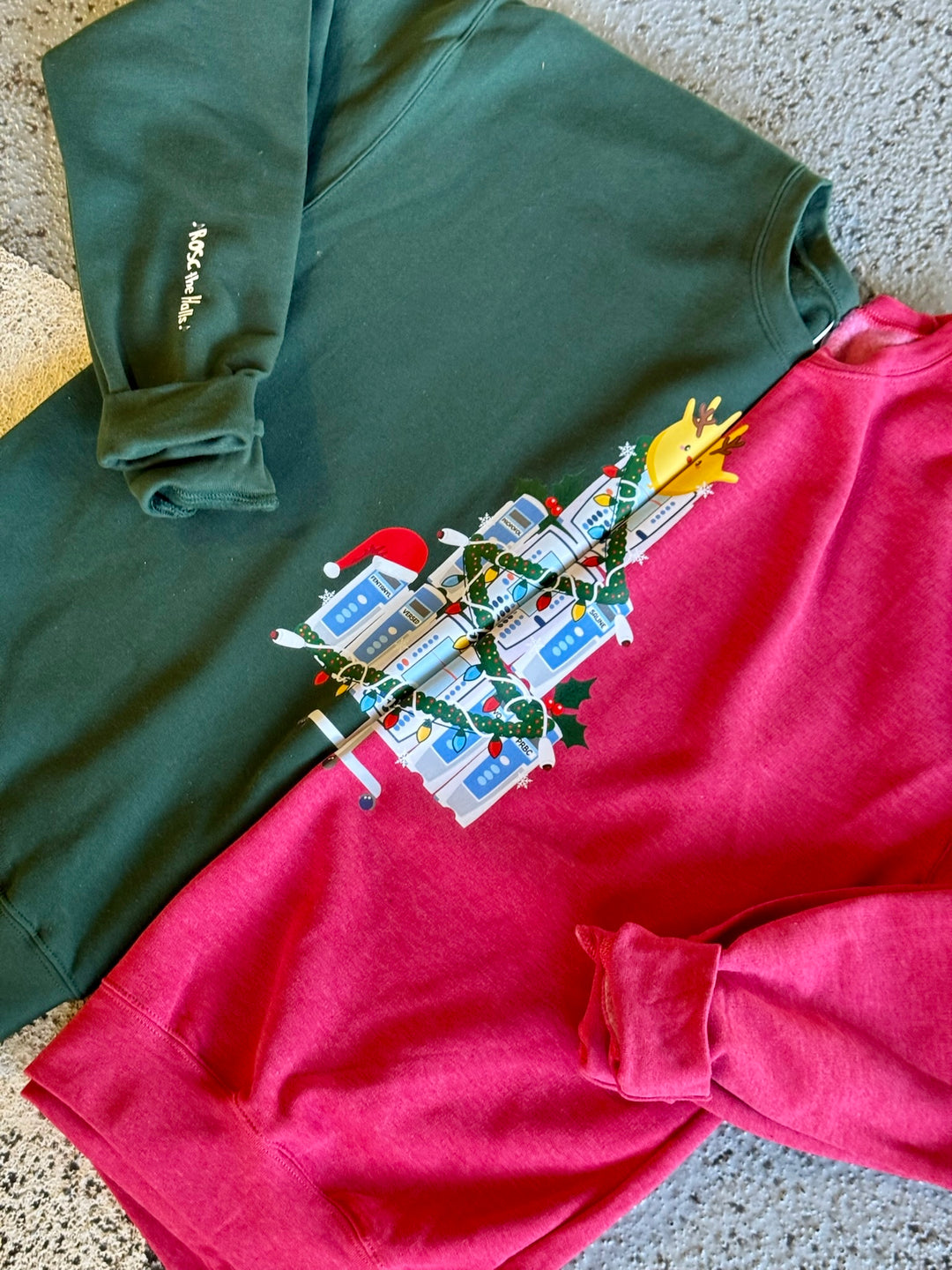 Green and red sweatshirts with IV Pump Christmas Tree design on a textured surface