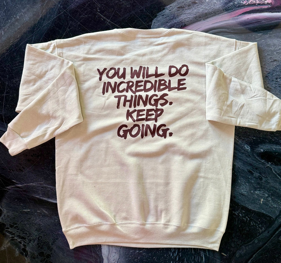 Back of sand-colored Incredible sweatshirt with motivational text on a dark textured surface