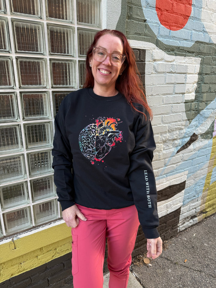 Ladyspinedoc wearing the black Synapse and Soul Anatomical Brain Heart Sweatshirt, with graphic half brain and half heart, and showing off the sleeve art that says "Lead with both"
