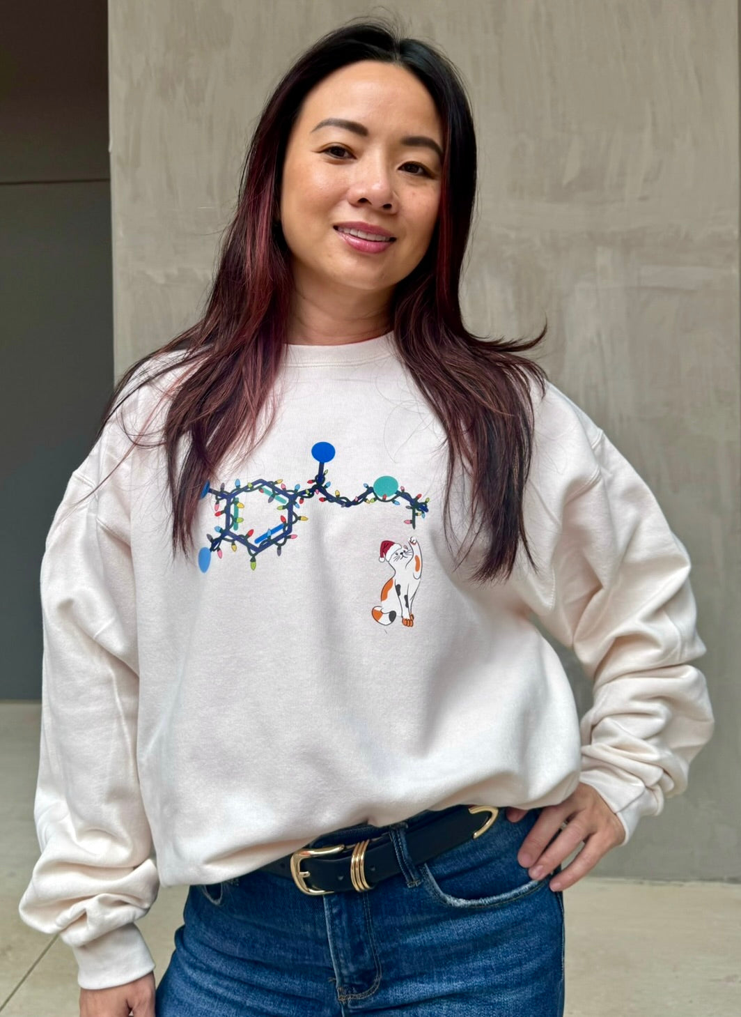 Person wearing a white sweatshirt with a colorful holiday adrenaline cat design, standing against a neutral background.