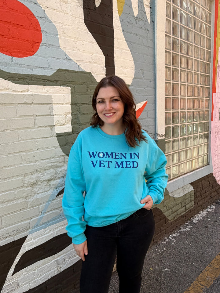 Woman outside wearing teal sweatshirt with 'Women in Vet Med' on the front