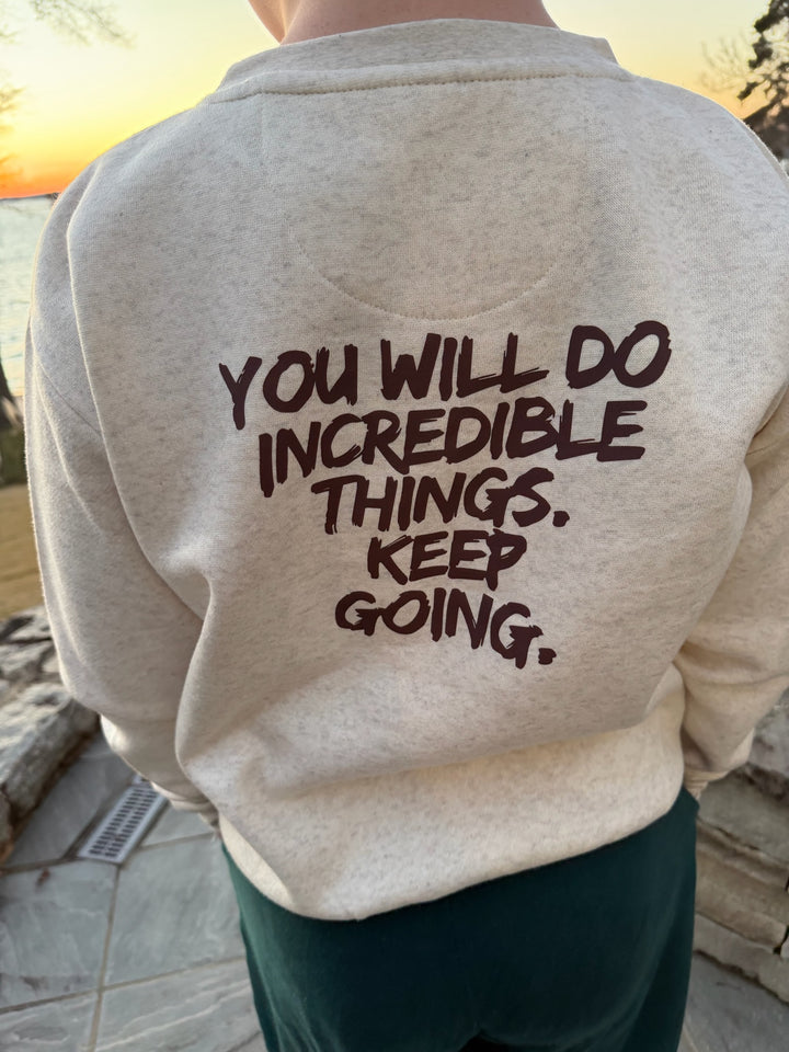 Youth wearing the Incredible Crewneck Youth Sweatshirt - Kids Natural Heather Shirt with Motivational "YOU WILL DO INCREDIBLE THINGS. KEEP GOING." motto, standing outdoors.