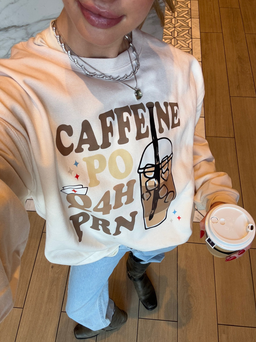 Smiling model showcasing close up view of the Perk Up Rx Crewneck Sweatshirt whie holding a coffee in her left hand. 
