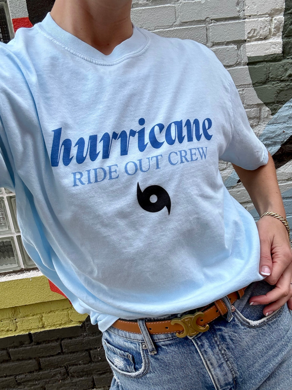 Person wearing a light blue t-shirt with 'hurricane RIDE OUT CREW' text and logo.