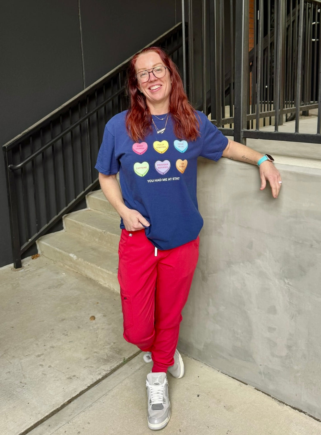 Ladyspinedoc wearing Navy Nurse Tee with Candy Hearts design and You Had Me At Stat text and red pants standing on a sidewalk.