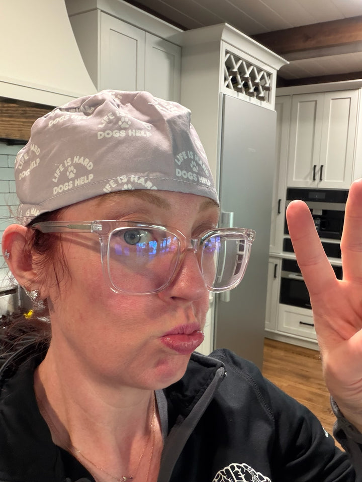 Ladyspinedoc wearing a gray scrub cap with Life Is Hard, Dogs Help logo and glasses in a kitchen