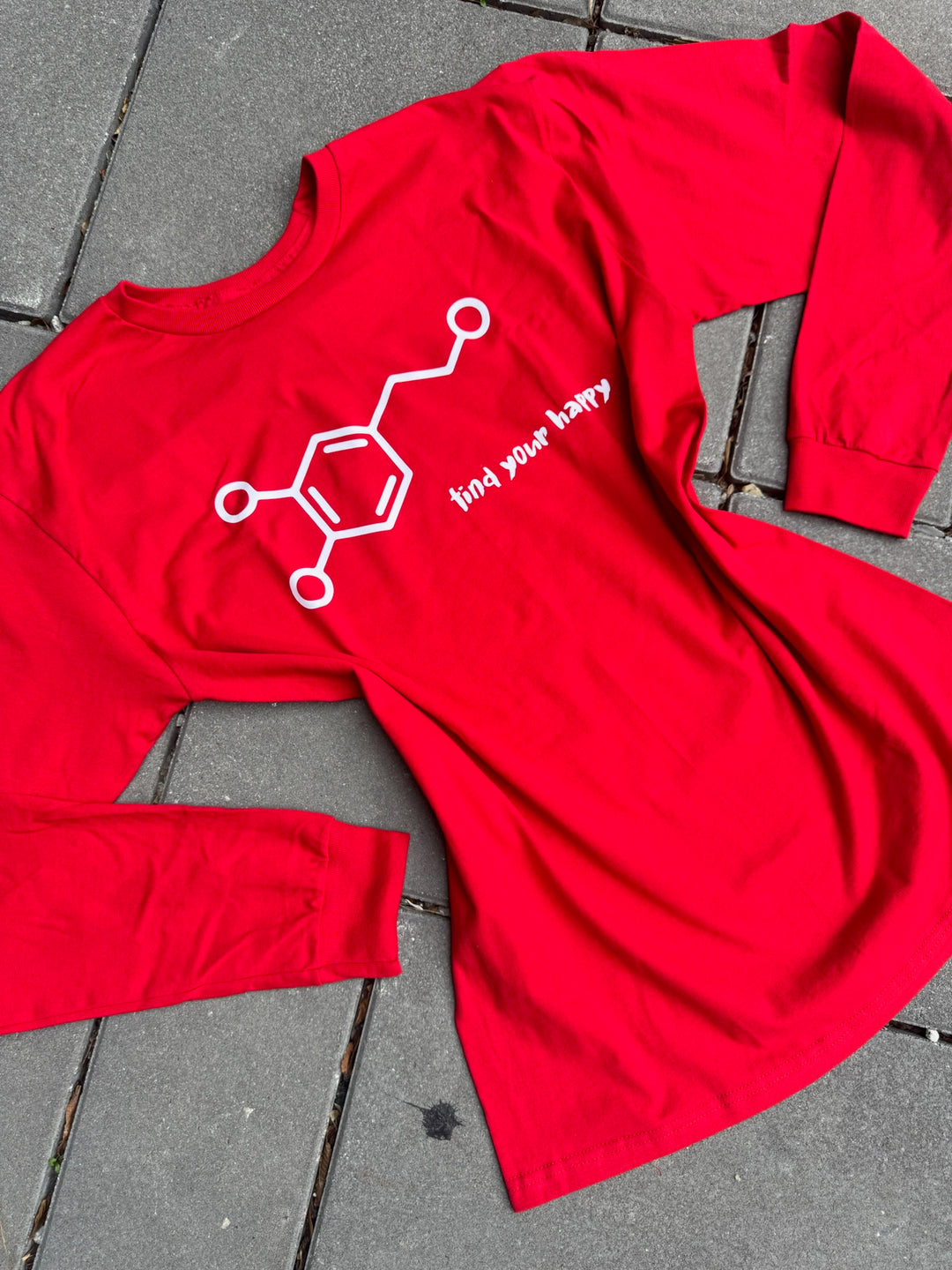Red long-sleeve shirt with a dopamine chemical structure graphic and find your happy text on a gray pavement background
