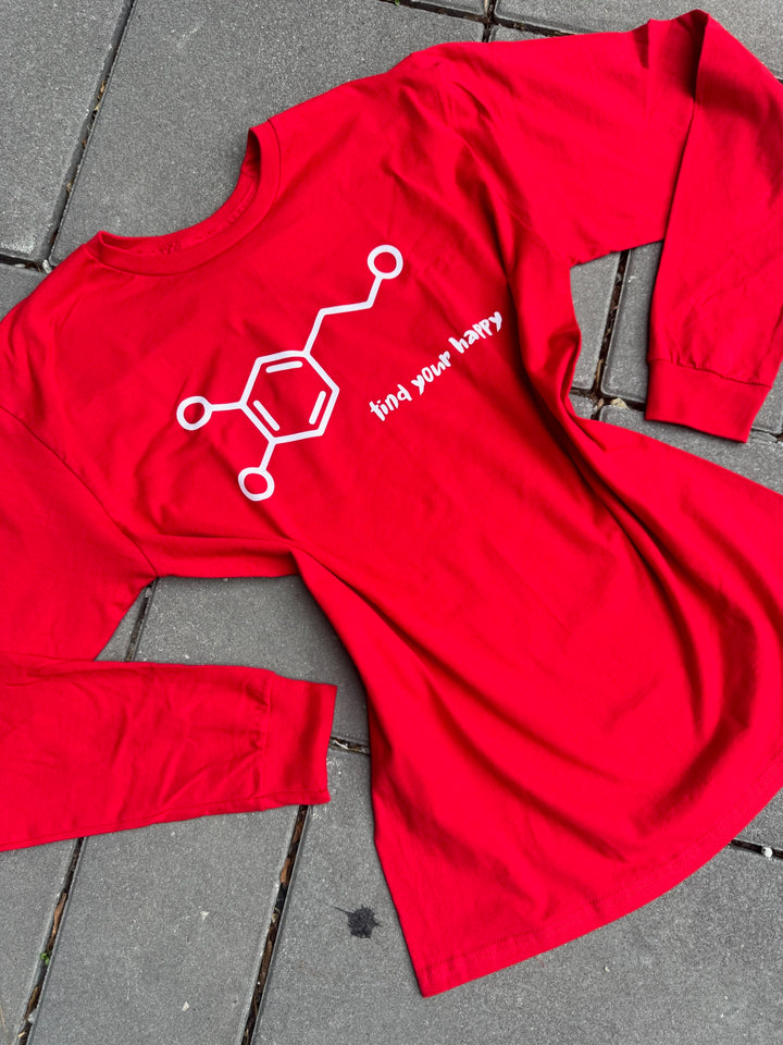 Red long-sleeve shirt with a dopamine chemical structure graphic and find your happy text on a gray pavement background
