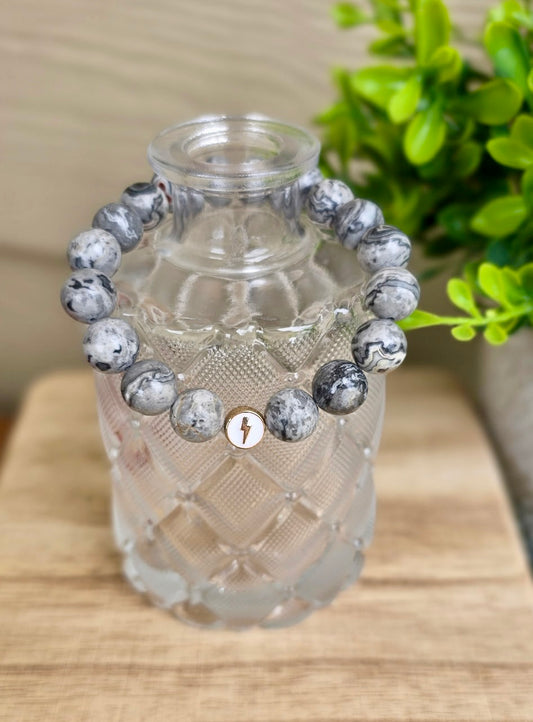 Glioblastoma Awareness Bracelet on a glass bottle and showing the gray Map Stone Jasper beads with one white enamel bead with gold lightning bolt.