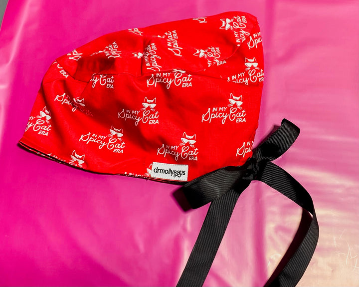 Red scrub hat with 'In My Spicy Cat' text on a pink background