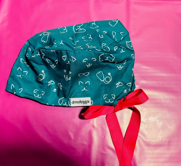 Green scrub cap with white patterns and a ribbon on a pink background