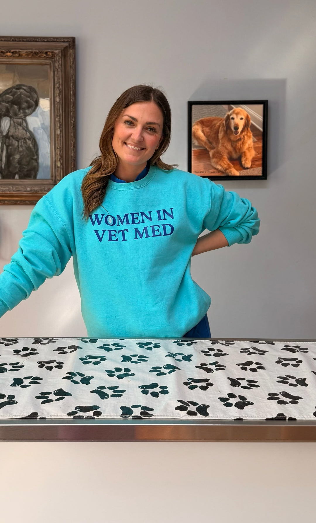 Dr Molly Brinkmann wearing a 'Women in Vet Med' sweatshirt in a veterinary setting with paw print table cover.