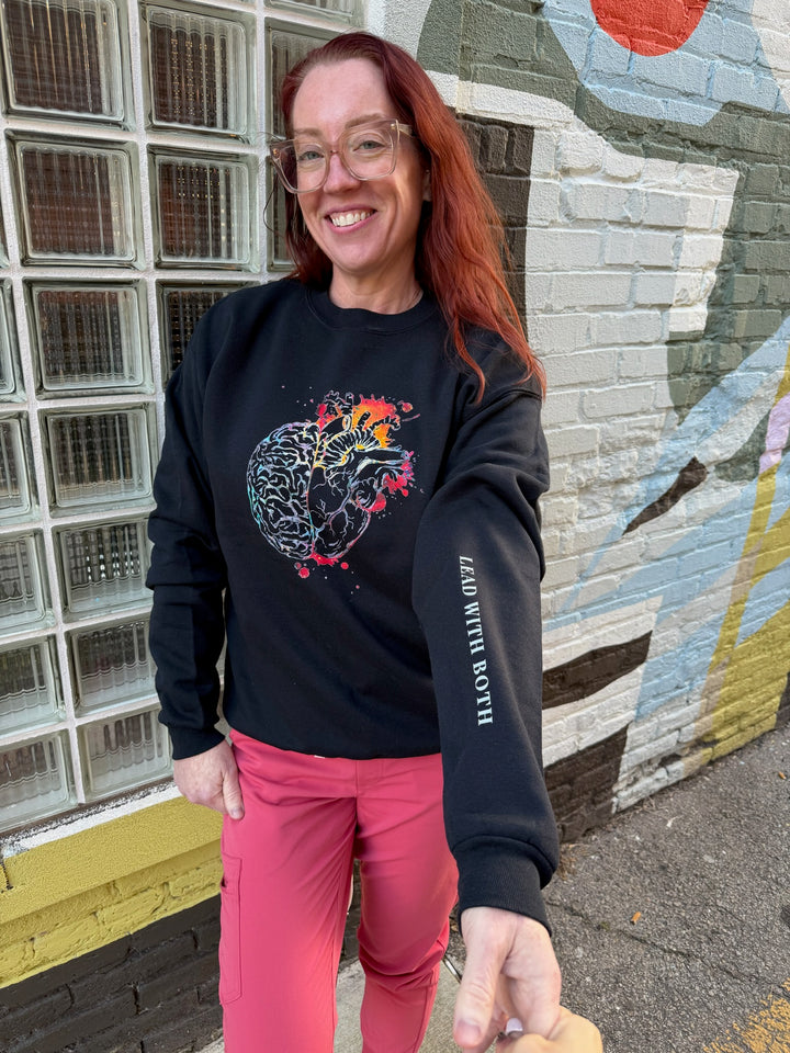 Ladyspinedoc wearing the black Synapse and Soul Anatomical Brain Heart Sweatshirt outside next to a wall mural