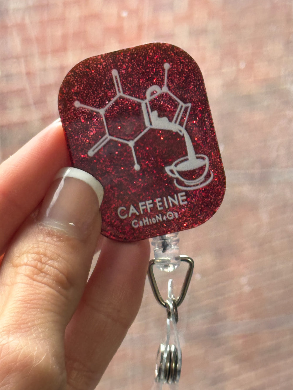 Woman holding Ladyspinedoc x Dr. Beachgem Red Sparkly Enerjava Badge Reel - Retractable with Alligator Clip and Caffeine Molecule Design on a dark red glitter background