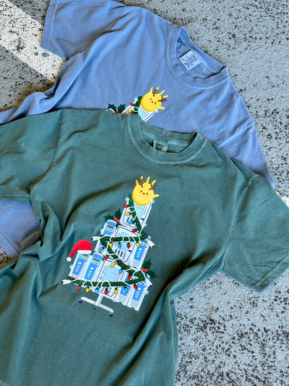 Two Nurse Christmas Tree Tee Shirts with IV Pump Design, one green and one blue, on a textured surface.