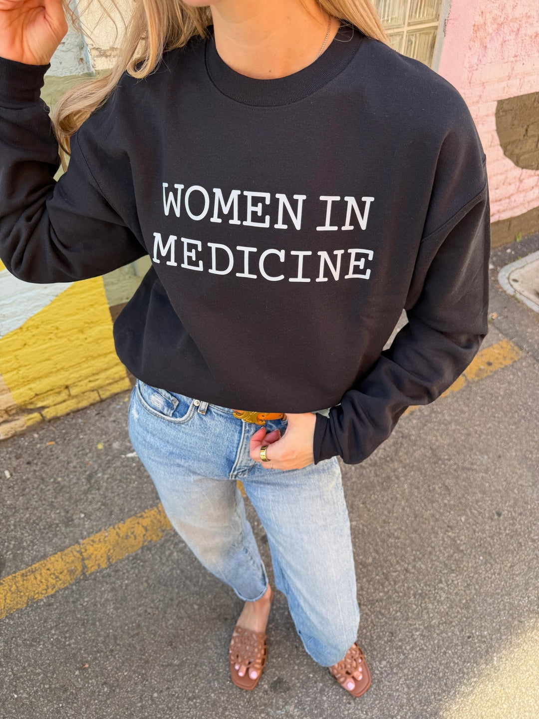 Person wearing a black sweatshirt with 'WOMEN IN MEDICINE' white text on a street.
