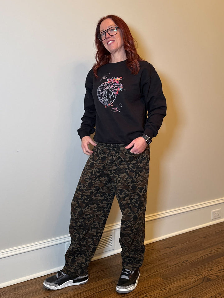 Ladyspinedoc wearing a black crewneck sweatshirt with a brain and heart design and the text 'Wisdom and passion' on it, paired with camouflage pants and sneakers.