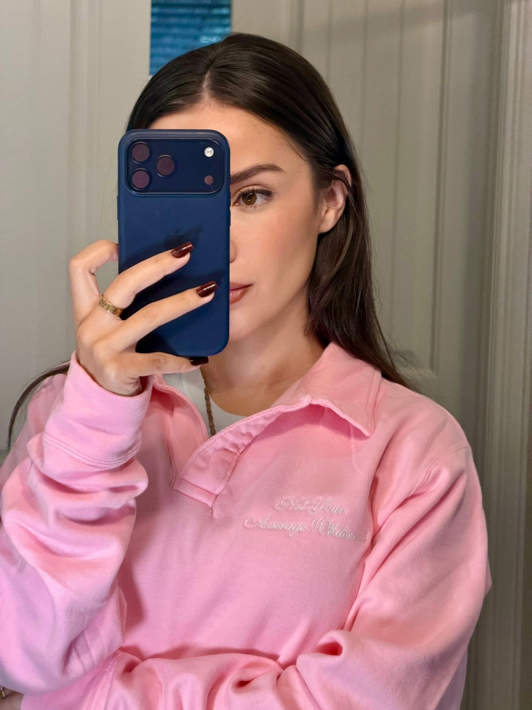 Dr Daisy wearing Embroidered 'Not Your Average Whitecoat' - Pink Polo Collar Sweatshirt holding a blue phone.